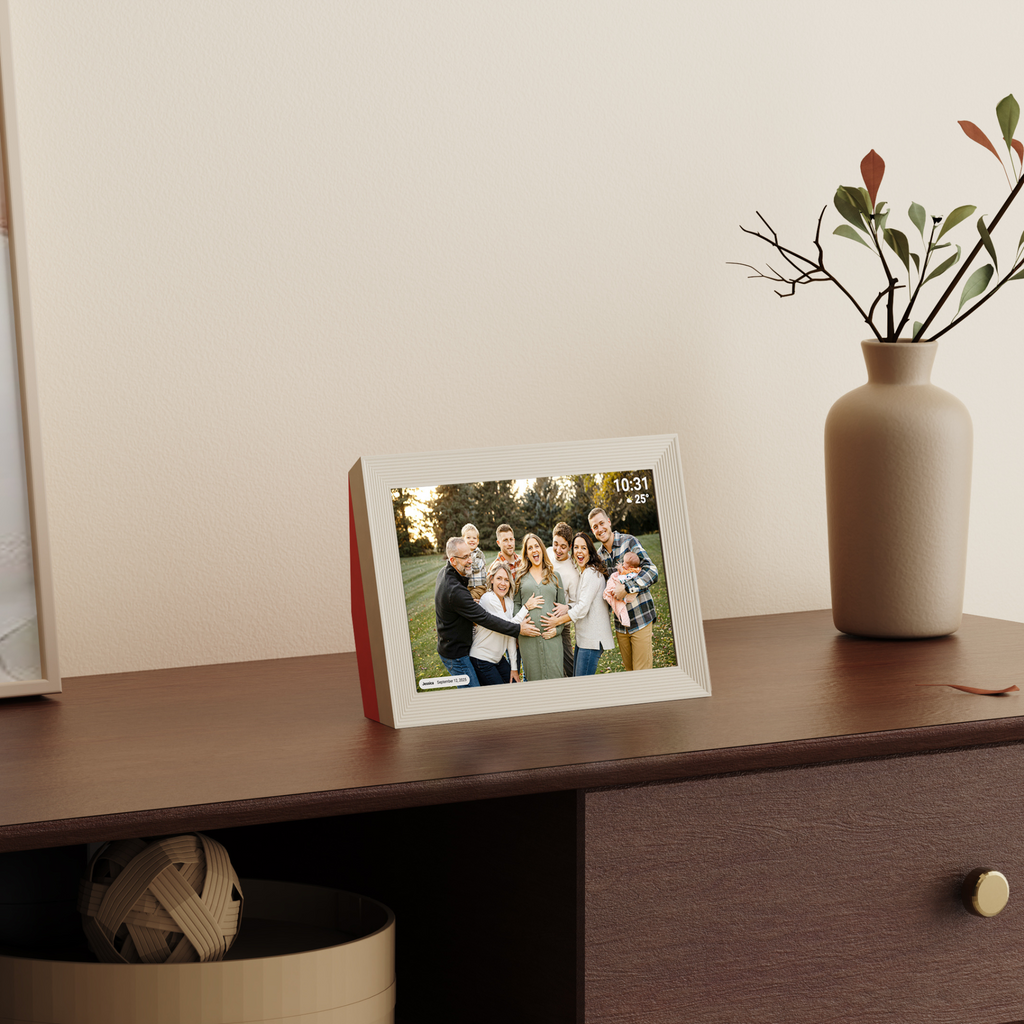 Digital photo frame displaying a family photo on a wooden surface with a vase in the background.