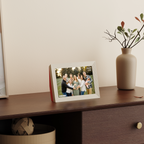Digital photo frame displaying a family photo on a wooden surface with a vase in the background.