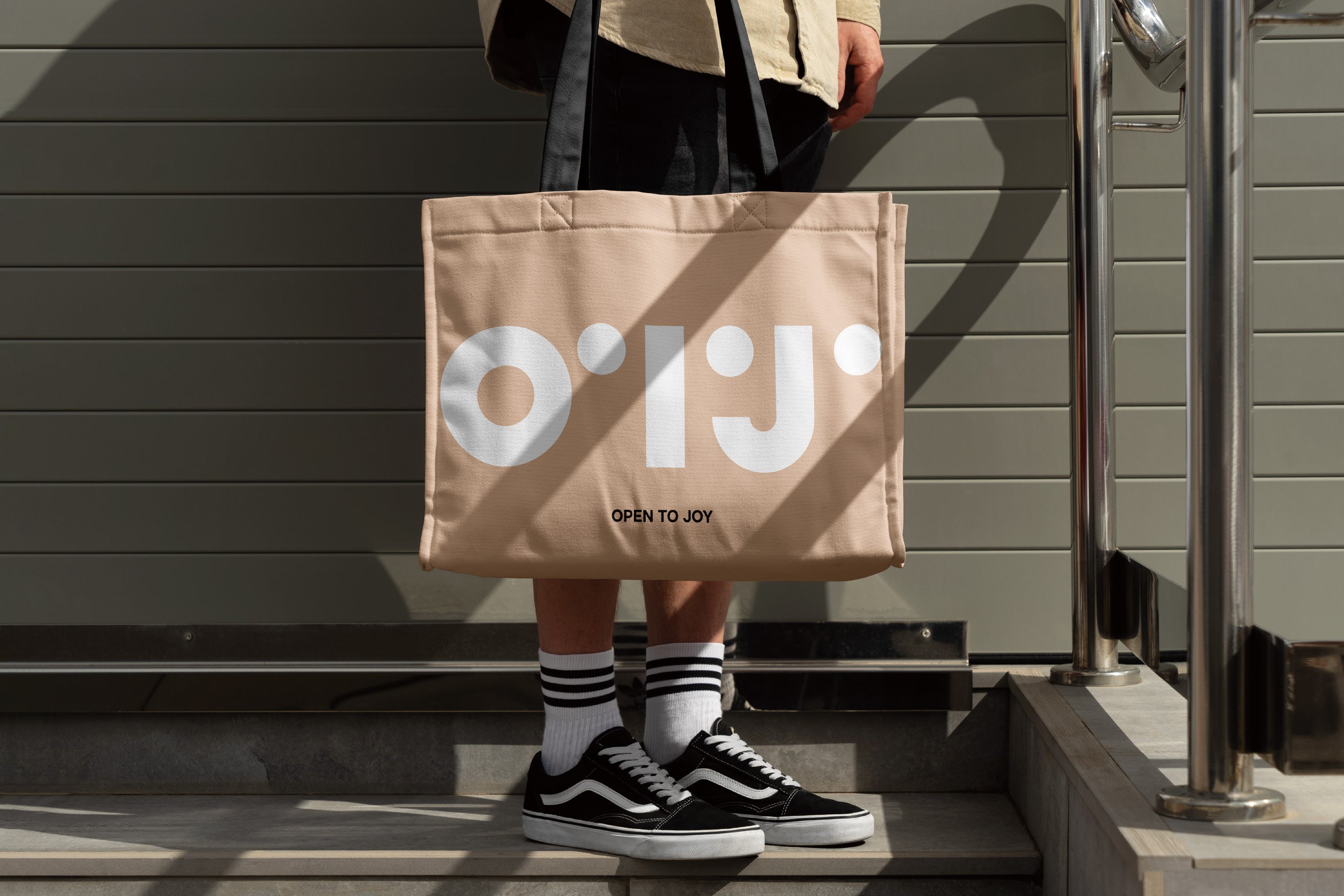 Person holding a beige tote bag with 'O'T'J' logo, standing on steps.