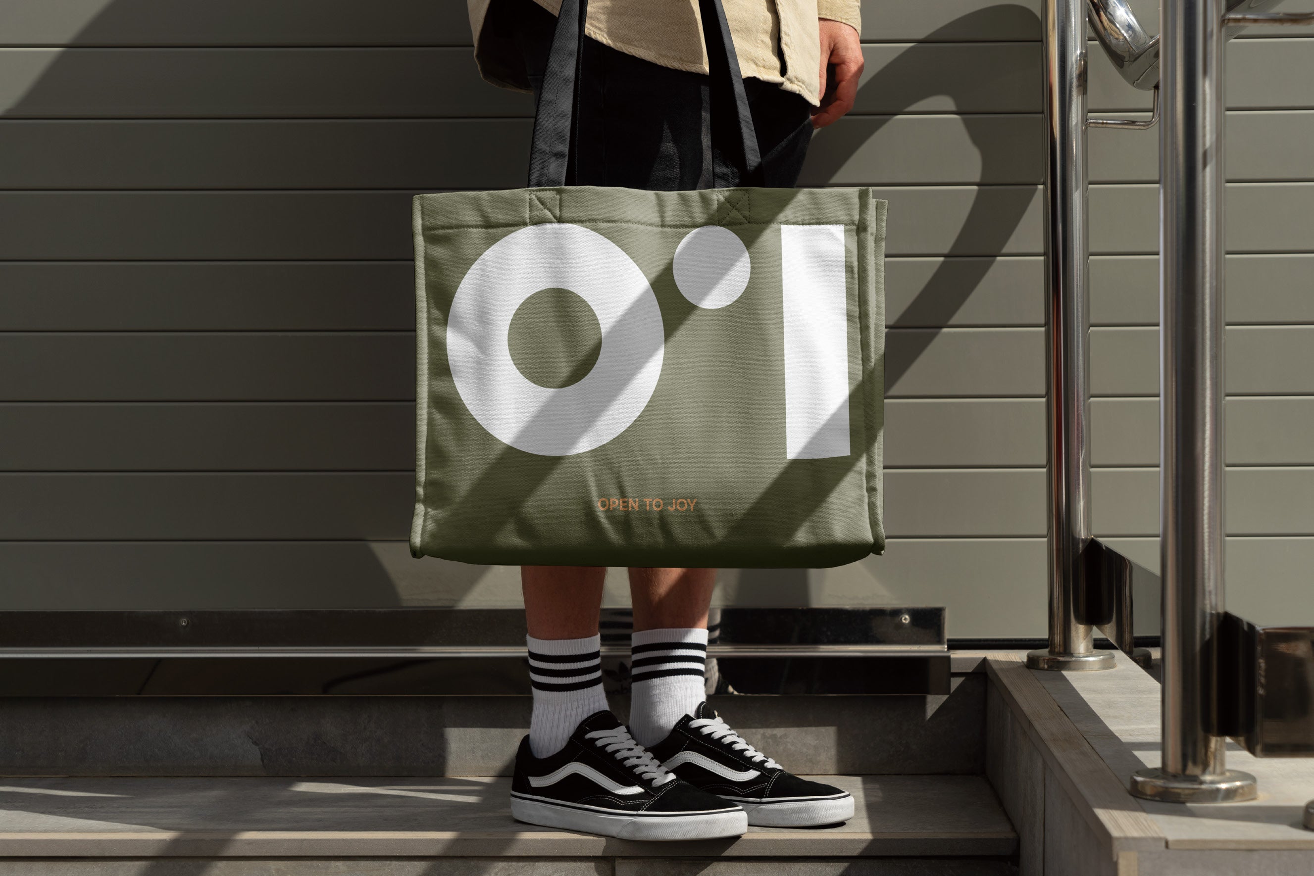 Person holding a green tote bag with a logo, standing on steps.