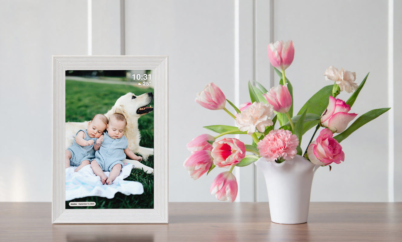 Digital photo frame displaying a family photo on a table with flowers and candles in the background.